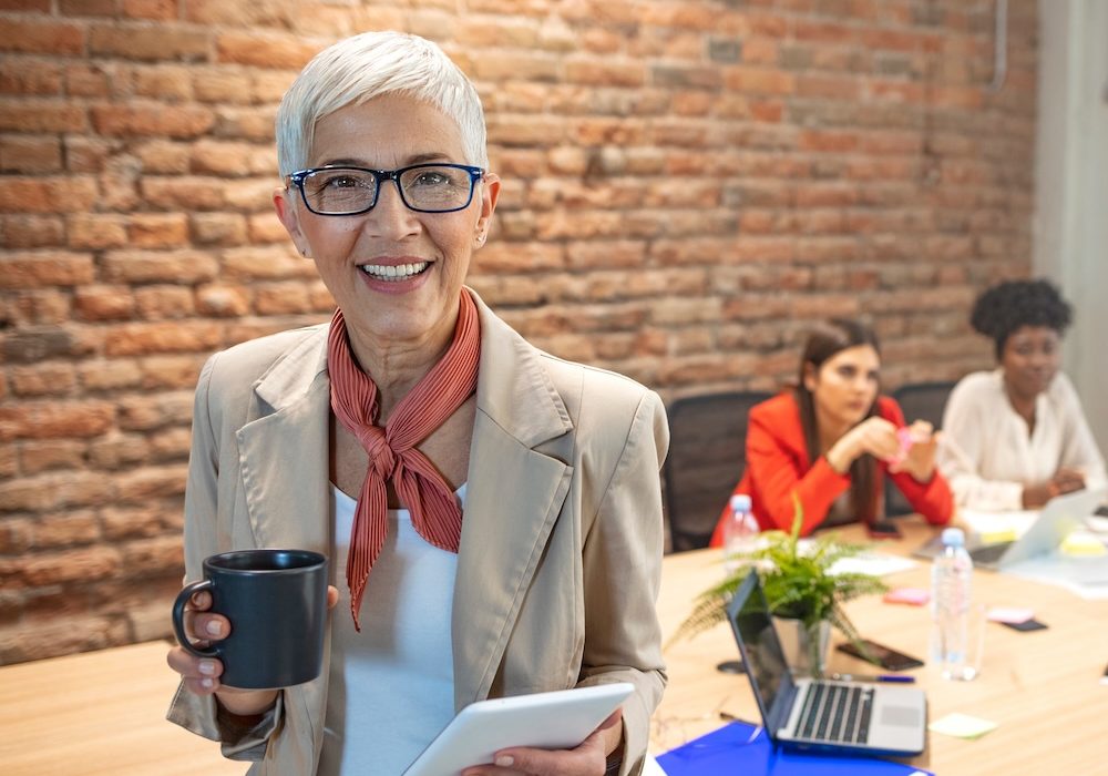 Portrait of a senior business woman on a good working day. Portrait Of Happy Senior Businesswoman In Office. Portrait of an executive professional mature businesswoman sitting on office desk